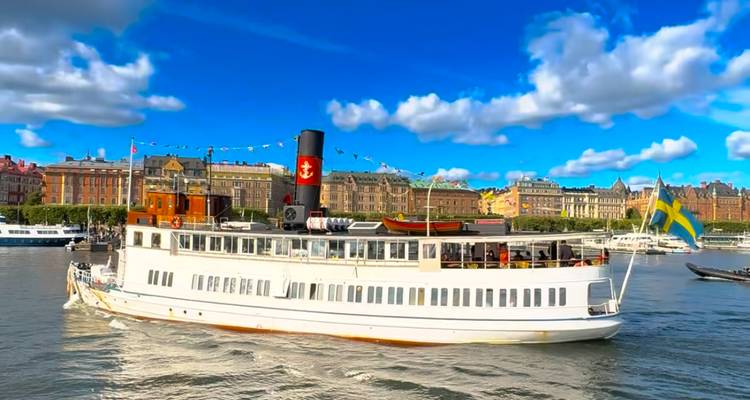 Bateau à vapeur historique blanc arborant le drapeau suédois naviguant le long du front de mer de Stockholm.
