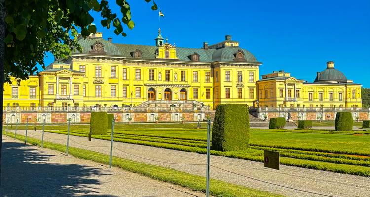 Vue ensoleillée du Palais de Drottningholm et de ses jardins formels sous un ciel bleu dégagé.