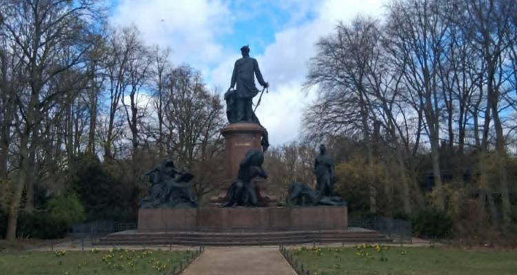 monument en bronze entouré d'arbres et de fleurs de printemps sous un ciel partiellement nuageux