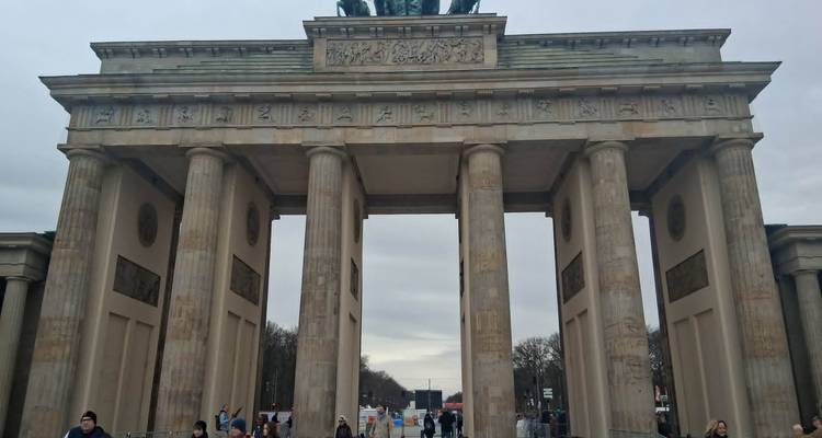 La porte de Brandebourg emblématique se dresse majestueusement sous un ciel gris tandis que les touristes se rassemblent sous ses colonnes.