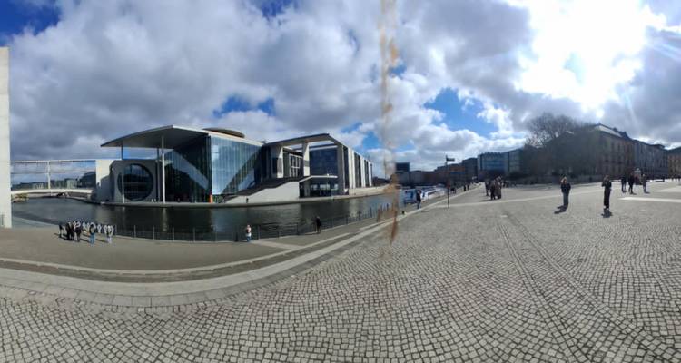Des bâtiments gouvernementaux modernes bordent la Spree par une journée partiellement nuageuse, avec des piétons sur la promenade.