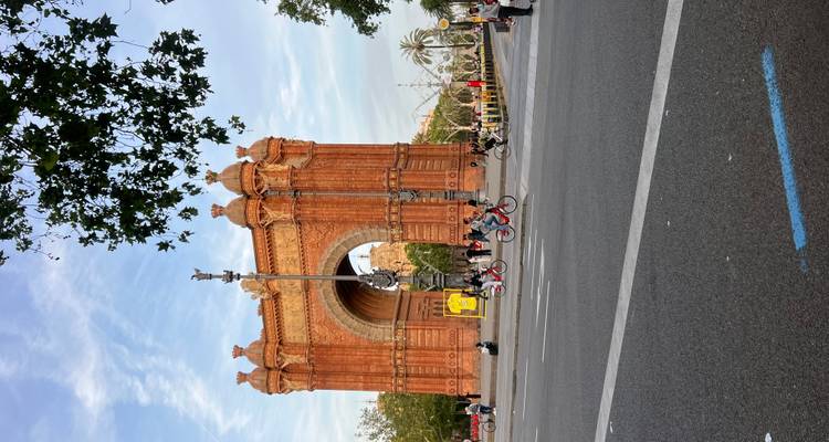 L'arc Arc de Triomf en briques rouges à Barcelone encadré par des arbres avec des cyclistes et des piétons passant au premier plan