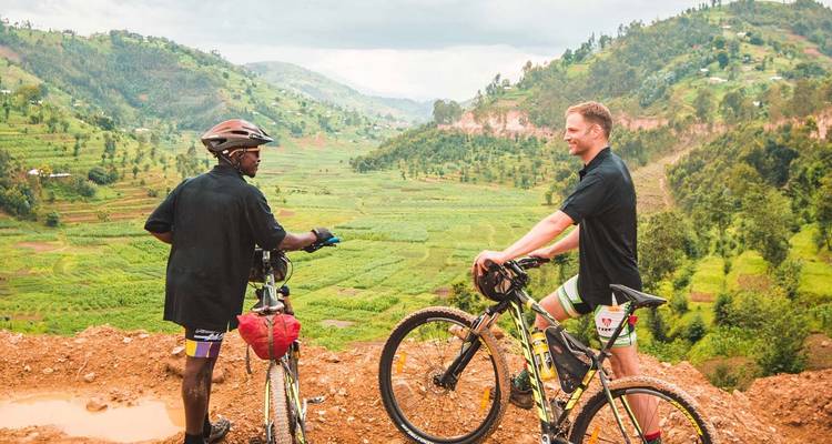 Deux cyclistes s'arrêtent pour discuter en surplombant des collines et des vallées en terrasses verdoyantes dans les zones rurales du Rwanda.