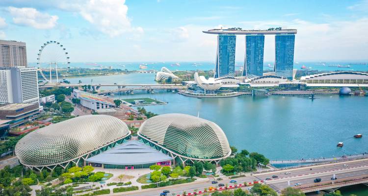 Panorama aérien de Marina Bay avec les dômes de l'Esplanade, la Singapore Flyer et Marina Bay Sands sur un ciel lumineux.