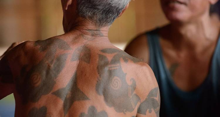 Vue rapprochée d'un dos tatoué présentant des motifs tribaux complexes lors d'une interaction villageoise