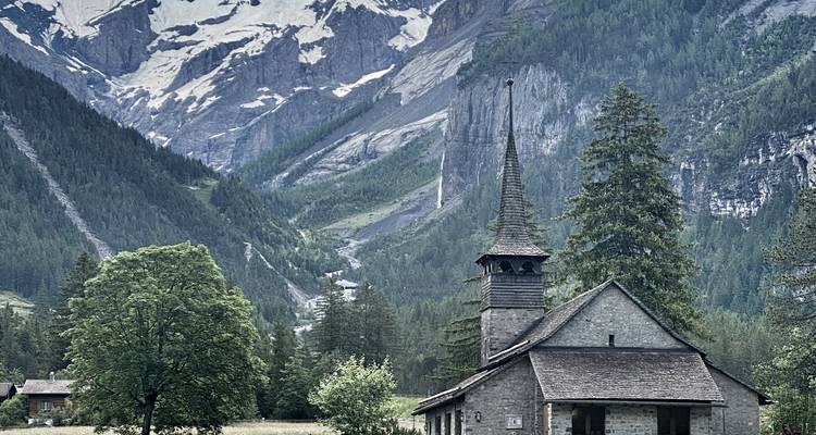 Petite chapelle alpine nichée dans une vallée verdoyante avec des falaises imposantes et une cascade en arrière-plan