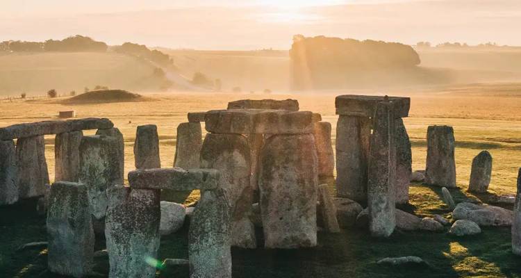 Mystérieux cercle de pierres de Stonehenge baigné dans la douce lumière de l'aube sur la campagne anglaise brumeuse.