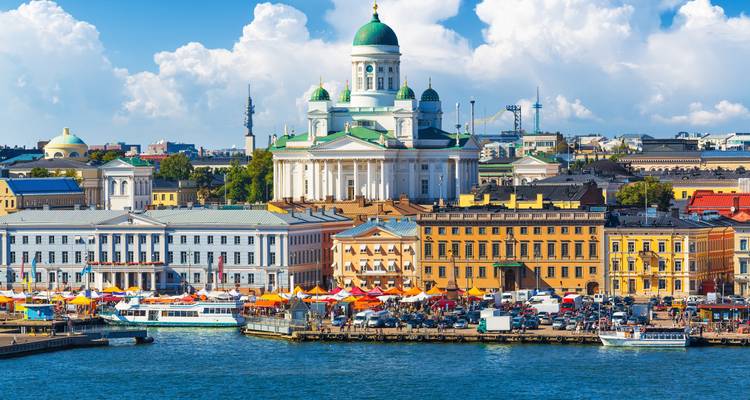 Cathédrale blanche emblématique d'Helsinki et bâtiments aux couleurs vives du marché en bord de mer vus de l'autre côté du port bleu.
