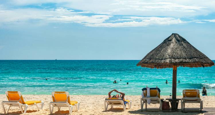 Scène relaxante de plage des Caraïbes avec des chaises longues jaunes, un parasol en chaume et des baigneurs profitant d'une eau turquoise cristalline.