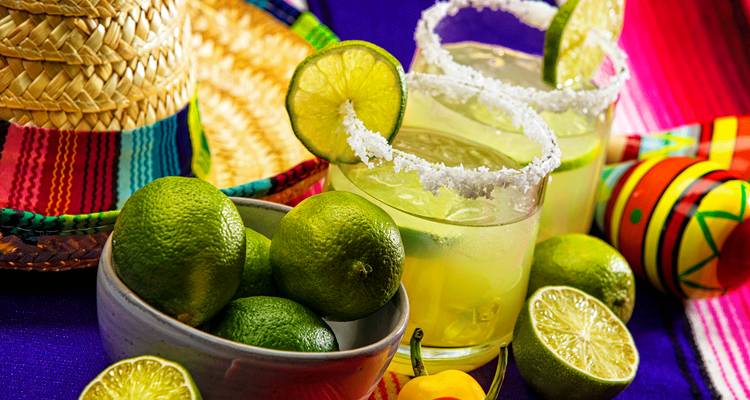 Nature morte mexicaine colorée avec des citrons verts frais, des verres à margarita bordés de sel, un sombrero et un tissu tissé vibrant.