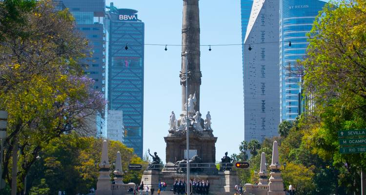 Le monument de l'Ange de l'Indépendance qui s'élève sur le Paseo de la Reforma, encadré par des gratte-ciel modernes et des arbres feuillus.