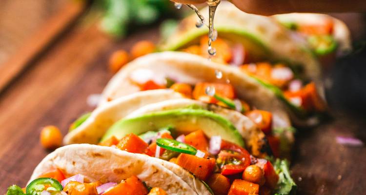 Gros plan de tacos aux légumes frais arrosés de jus de citron vert sur une planche en bois.