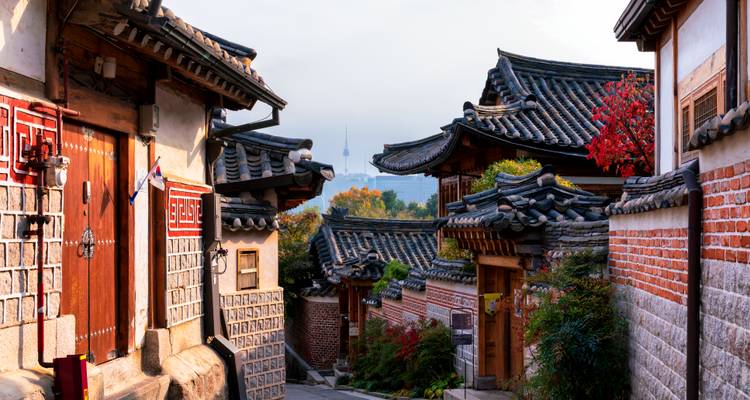 Ruelle hanok traditionnelle aux toits carrelés et au feuillage automnal encadrant la N Tower de Séoul au loin.
