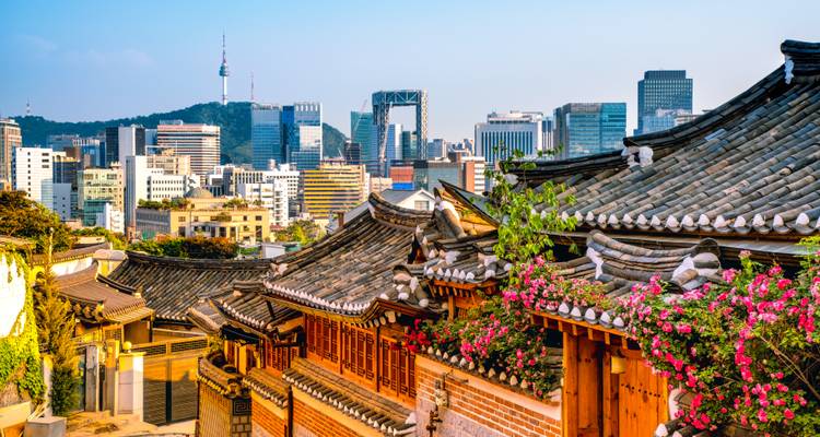 Los tejados tradicionales con azulejos del Pueblo de Hanok de Bukchon con el skyline moderno de Seúl elevándose detrás.