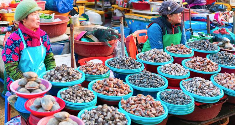 Las mujeres venden una variedad de mariscos exhibidos en tazones coloridos en un mercado de mariscos al aire libre muy concurrido.
