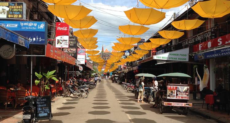 A lively street in Siem Reap is covered by hanging yellow umbrellas above cafés and tuk-tuks.