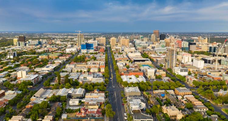 Vista aérea elevada de las calles en cuadrícula de Adelaida bordeadas de árboles que conducen a un horizonte moderno bajo un cielo azul