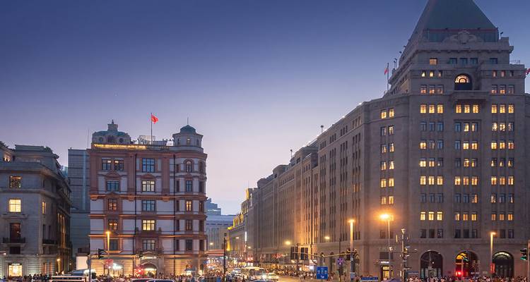 Les lumières du soir illuminent les bâtiments historiques le long du Bund de Shanghai tandis que la circulation et les piétons remplissent la rue au crépuscule.