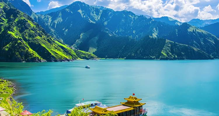 Lago alpino de un azul brillante rodeado de empinadas montañas verdes y un pabellón chino tradicional.