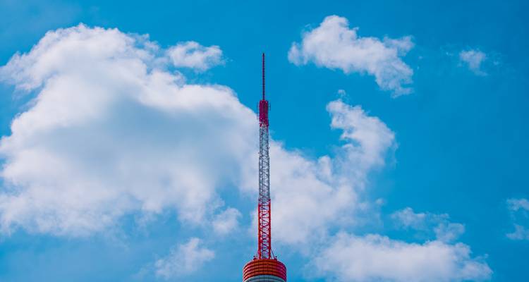 Gros plan d'un grand mât de radio rouge et blanc se détachant sur un ciel bleu clair parsemé de nuages.