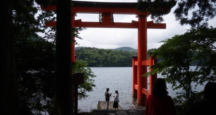 Un grand portique rouge torii se dresse à la lisière d'un lac tranquille entouré de collines boisées.