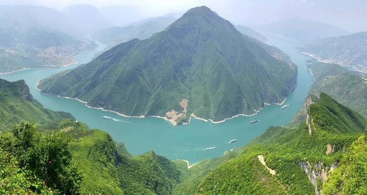 Vista aérea panorámica de una enorme montaña verde rodeada por el río Yangtze de color turquesa que serpentea alrededor.