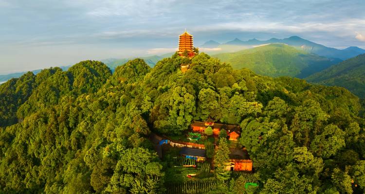 Una pagoda corona una cresta de montaña densamente boscosa bajo la suave luz de la tarde.