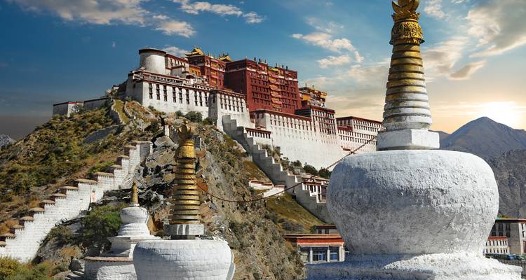 Der majestätische Potala-Palast thront auf einem felsigen Hügel mit einer goldenen Stupa im Vordergrund zur goldenen Stunde.