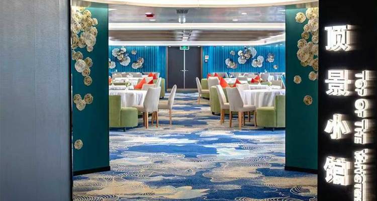 Eingang zum stilvollen Restaurantbereich eines Kreuzfahrtschiffes mit gemustertem Teppich und blaugrünen Wänden.