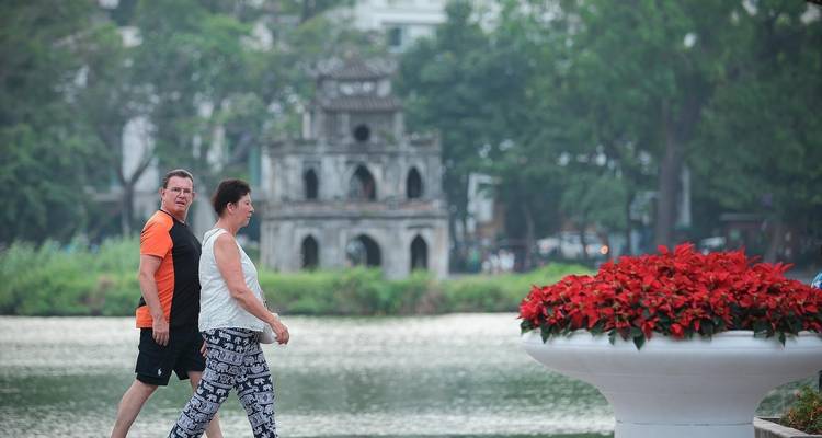Les touristes se promenant autour du lac Hoan Kiem avec la tour ancienne en arrière-plan et des jardinières de fleurs.