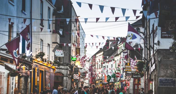 Rue étroite et animée à Galway ornée de guirlandes et de drapeaux au-dessus des foules du soir.