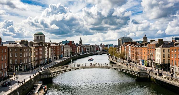 Vue panoramique sur la rivière Liffey de Dublin avec le pont Ha'penny et les bâtiments historiques bordant les deux rives sous des nuages dramatiques