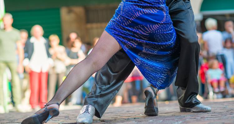 Primer plano de las piernas de bailarines de tango actuando apasionadamente en una calle de la ciudad.