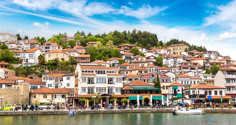 Farbenfrohe Häuser an den Hängen von Ohrid mit Blick auf die lebendige Seeuferpromenade voller Menschen
