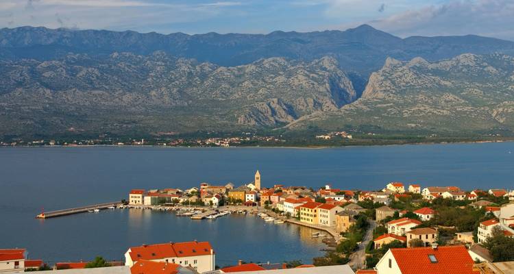 Village côtier pittoresque aux toits rouges donnant sur une baie calme, encadré par des montagnes calcaires spectaculaires en Croatie