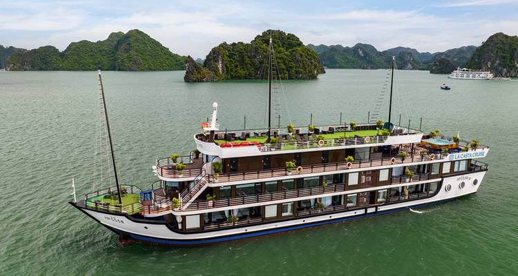 Navire de croisière blanc à trois ponts naviguant dans des eaux vertes et calmes parsemées d'îles calcaires