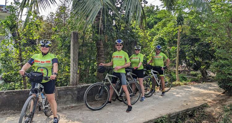 Radsportgruppe in übereinstimmenden grünen Trikots macht eine Pause neben üppiger Vegetation auf einem ländlichen Weg.