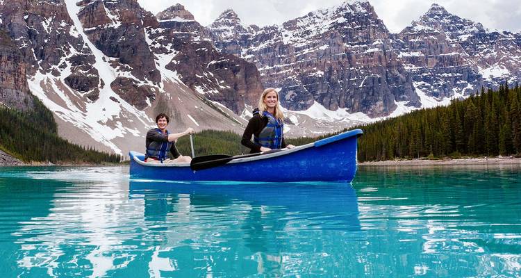 Deux femmes pagaient un canoë bleu vif sur un lac de glacier turquoise entouré de pics imposants couverts de neige.