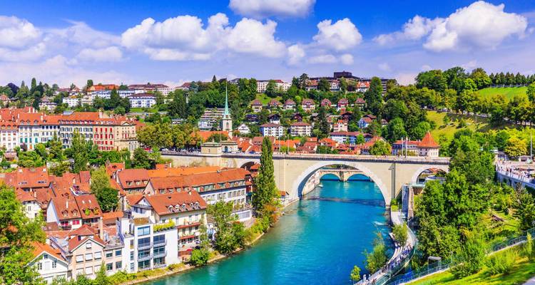 Vue panoramique de la vieille ville de Berne avec ses maisons aux toits rouges, son pont en arche et la rivière Aare turquoise.