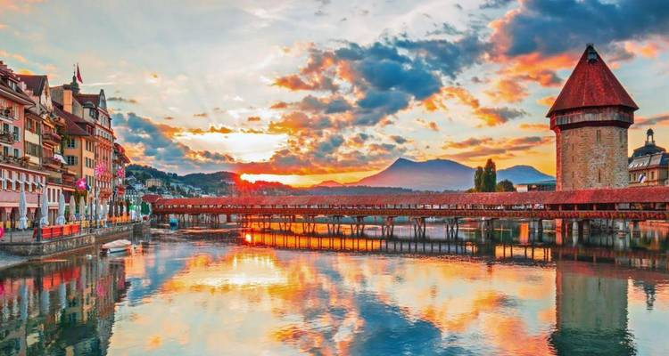 La lumière du coucher de soleil se reflétant sur le Pont de la Chapelle de Lucerne, la tour d'eau et les bâtiments colorés du front de mer.