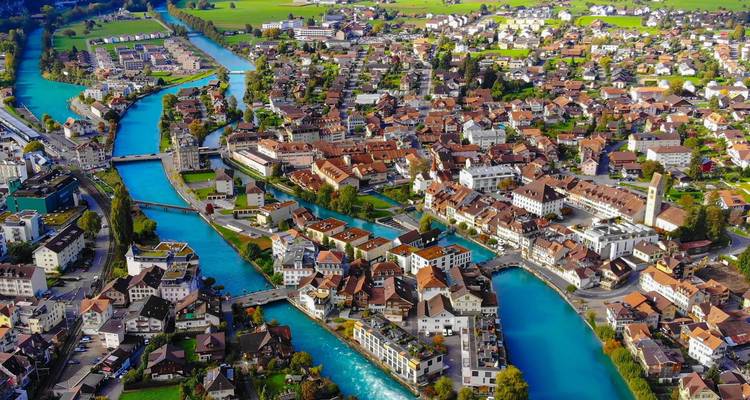 Vue aérienne panoramique d'Interlaken avec des rivières turquoise qui divisent la ville et des champs verts au-delà.