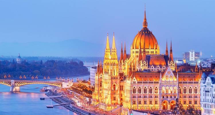Bâtiment du Parlement hongrois illuminé brillant au crépuscule à côté du Danube.