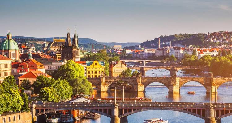 Plusieurs ponts historiques enjambant la rivière Vltava de Prague avec les flèches de la ville illuminées par la lumière chaude de l'après-midi.