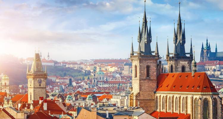 Les flèches gothiques de la vieille ville de Prague avec les toits illuminés par le soleil et le château au loin.