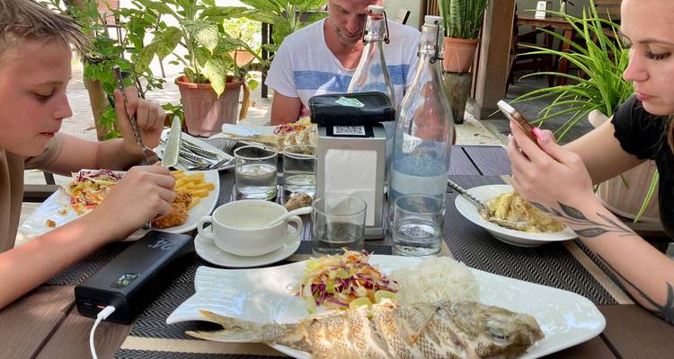 Famille mangeant du poisson entier grillé, des frites et une salade à une table de restaurant en plein air.