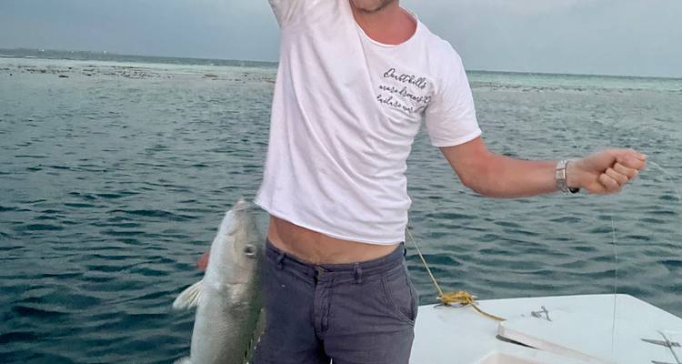Homme souriant sur un bateau tenant un gros poisson fraîchement pêché devant un paysage de mer ouverte.