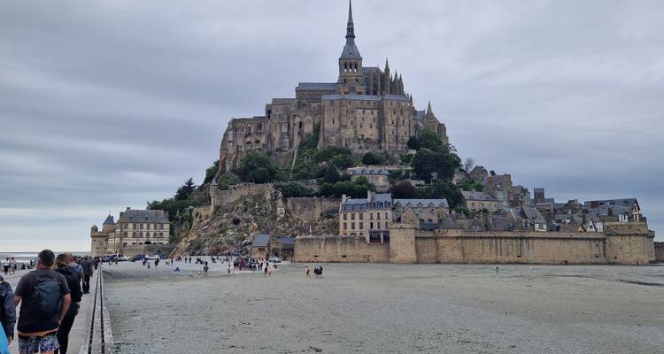 L'emblématique abbaye du Mont-Saint-Michel s'élevant au-dessus des plats vaseux des marées avec des visiteurs marchant sur la chaussée.