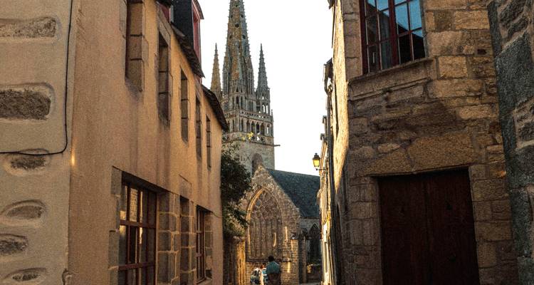 Ruelle en pierre étroite menant à une flèche de cathédrale majestueuse à l'heure dorée avec un promeneur solitaire.