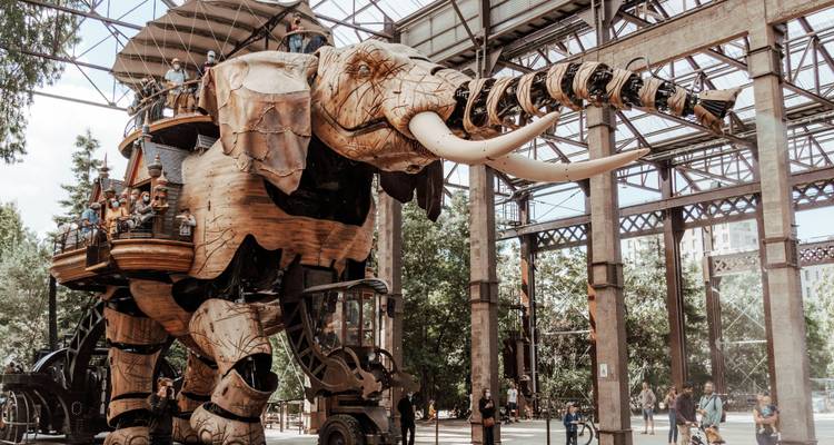 Éléphant mécanique géant transportant des passagers à l'intérieur d'un hall industriel en verre et acier à Nantes.