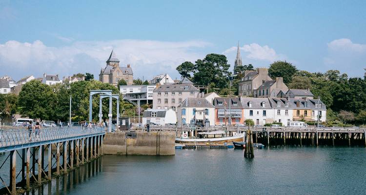 Port de charme avec une jetée en bois, des bateaux amarrés et une skyline pittoresque du village breton sous un ciel ensoleillé.
